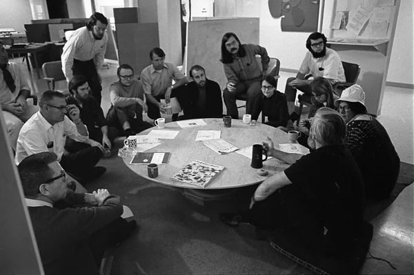 The Augmentation Research Center team sitting in a circle around a low round table, papers and coffee mugs between them.